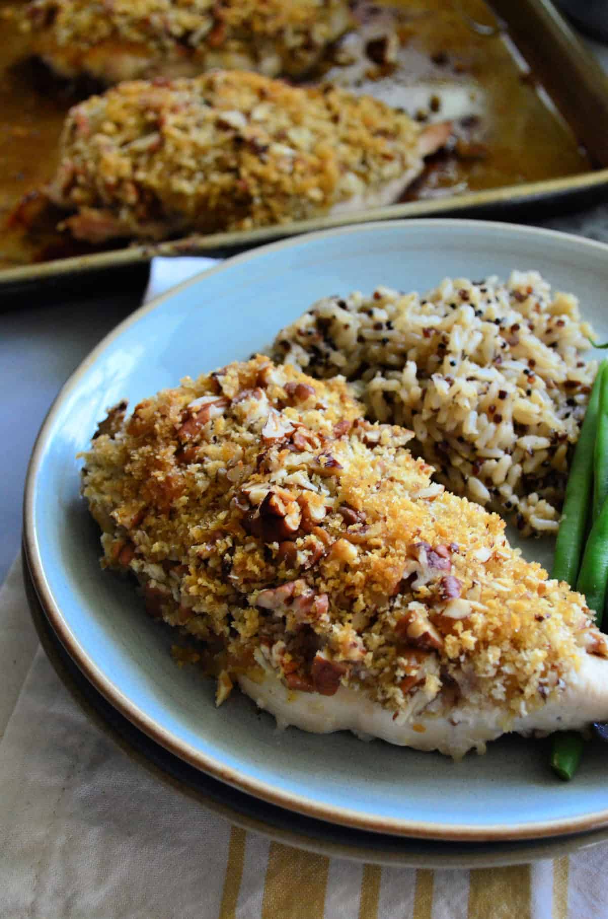 Light blue plate with a close up of pecan chicken with rice and green beans.