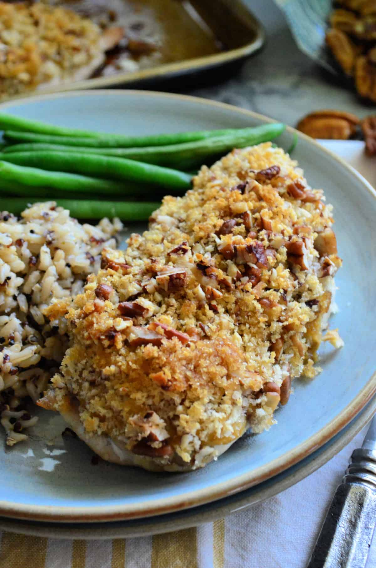 Close up of side view pecan crusted chicken breast served with green beans.