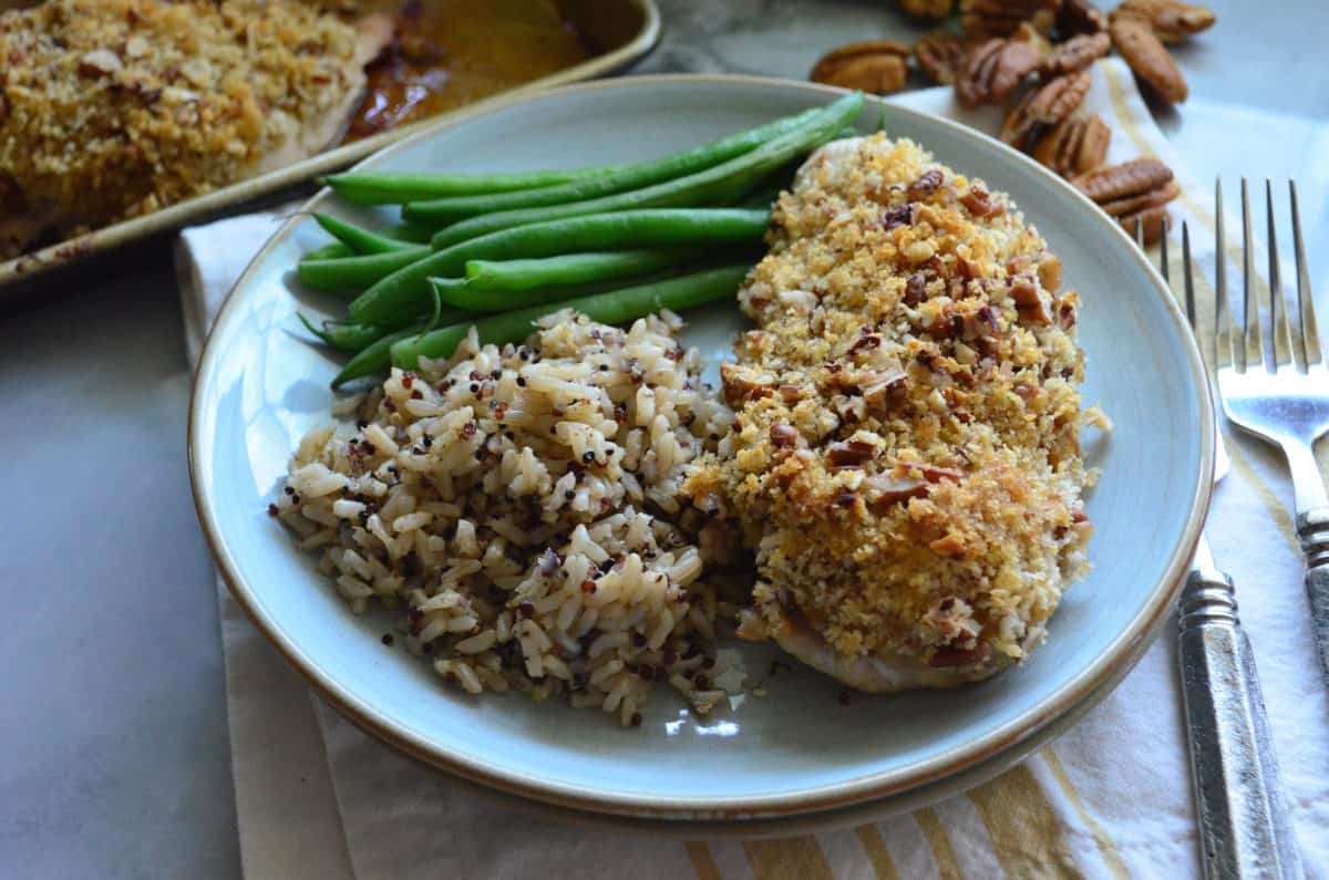 Light blue plate, pecan chicken, wild rice, green beans with pecans and a sheet pan in background.