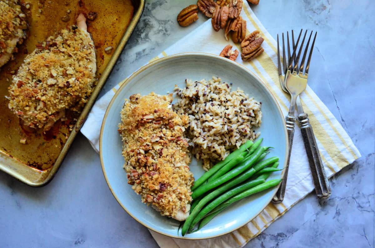 Light blue plate with pecan chicken, green beans, wild rice and 2 forks next to the plate.