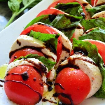 Close up of lined up tomato, basil, mozzarella drizzled with oil and balsamic vinegar.
