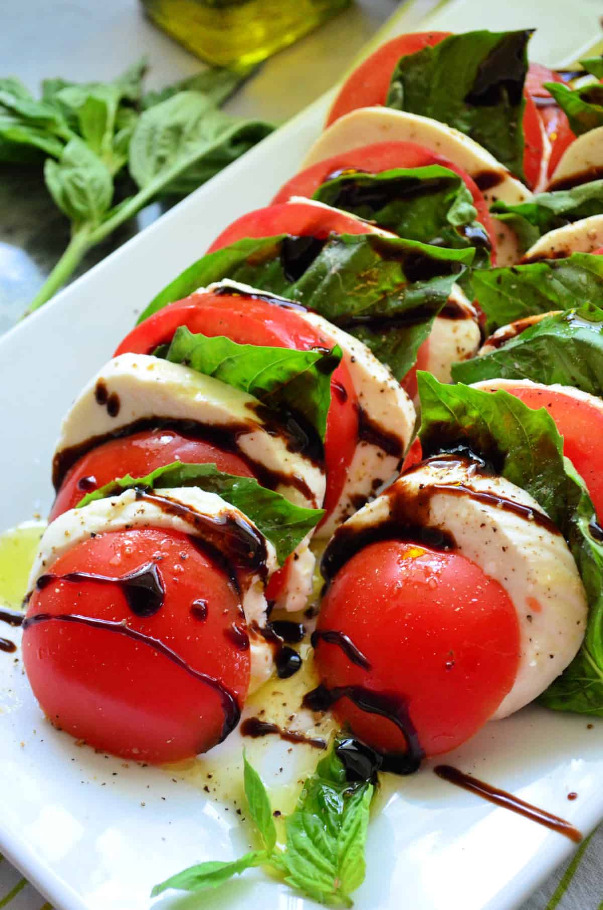 Close up of lined up tomato, basil, mozzarella drizzled with oil and balsamic vinegar.