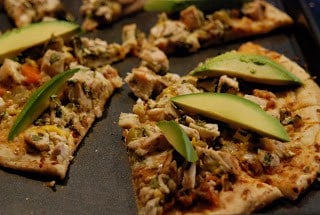 Thin crust pizza with chicken and cheese and slices of avocados. 