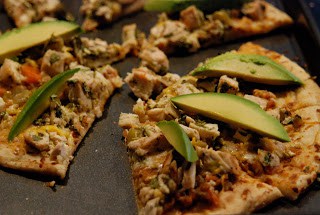 Thin crust pizza with chicken and cheese and slices of avocados.