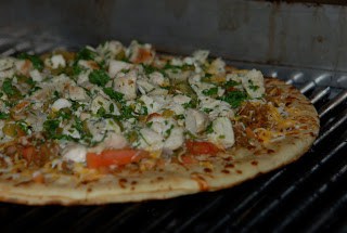 Thin crust pizza loaded with chicken and cilantro on a grill.