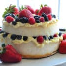 layered angel cake with mixed berries in middle layer and as topping on white cakestand.
