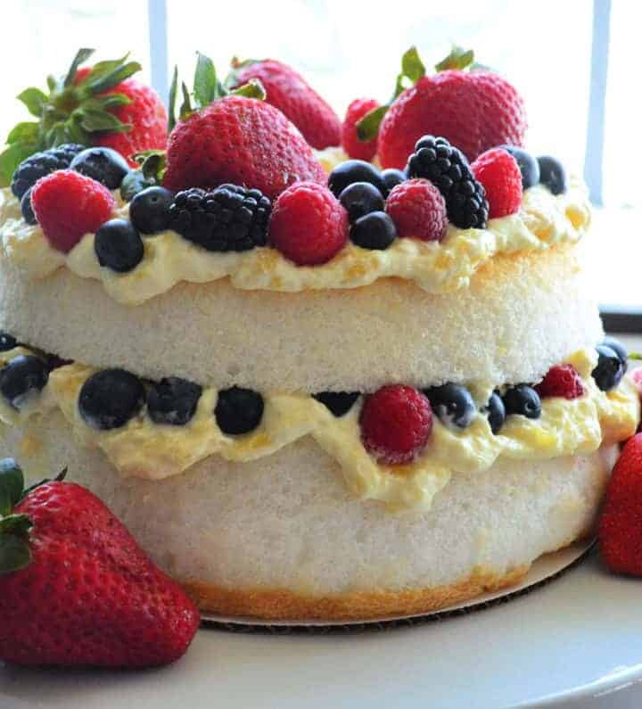 layered angel cake with mixed berries in middle layer and as topping on white cakestand.