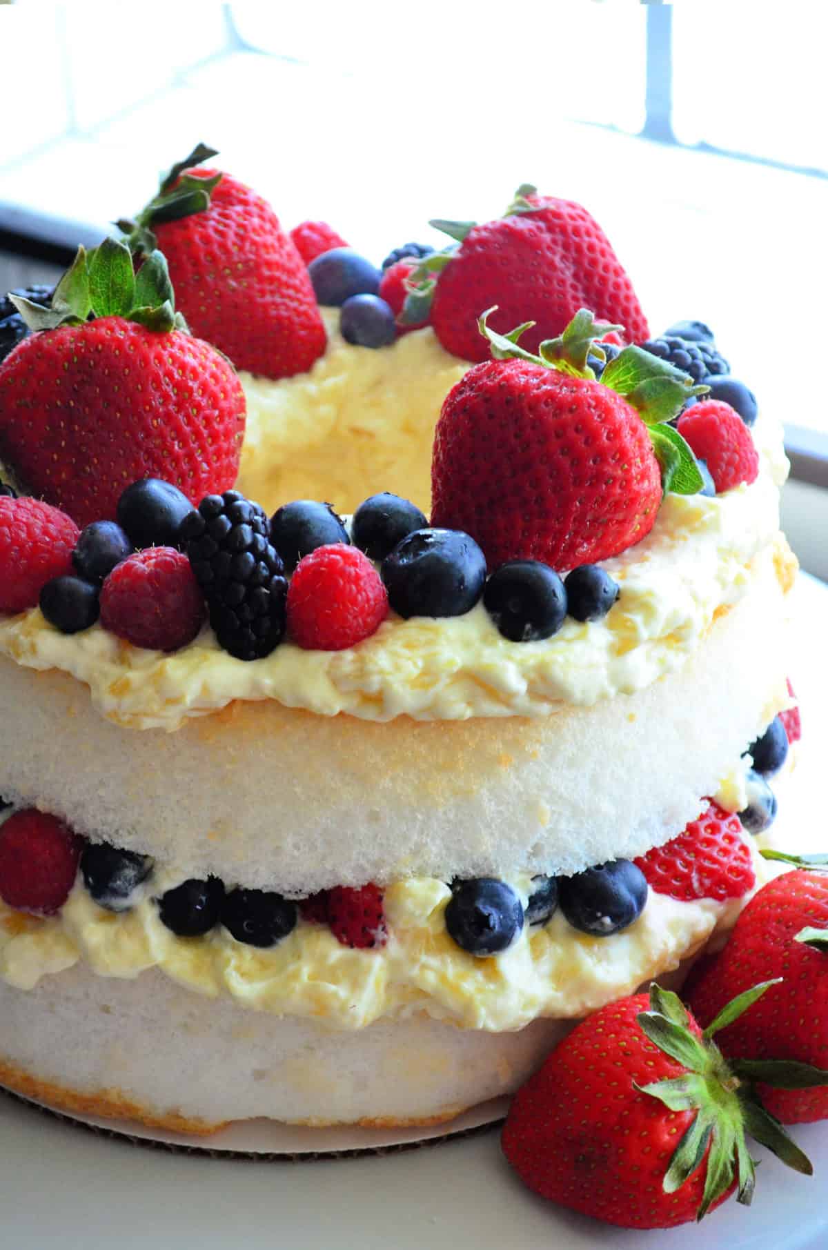 Side view of layered angel cake with mixed berries in middle layer and as topping.