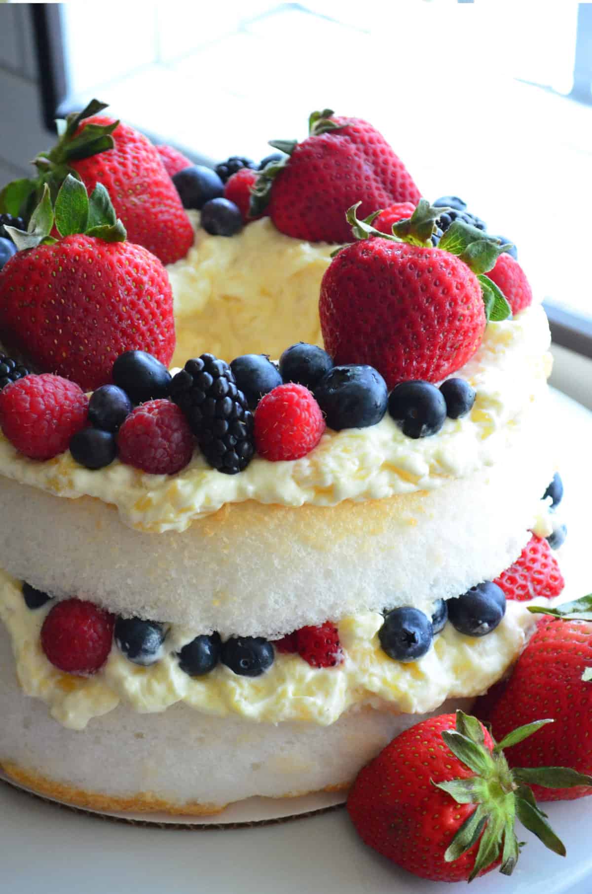 Close up of a layered cake with cream and berries on a white cake stand.