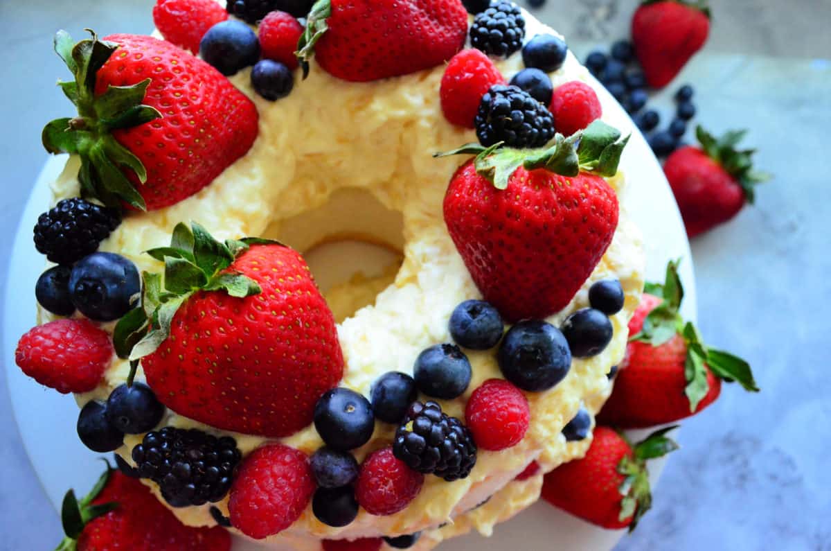 Top view of circular cake with hole in center topped with white icing and mixed berries.