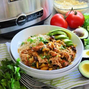 Chicken and black beans with rice and avocado, all in a white plate.