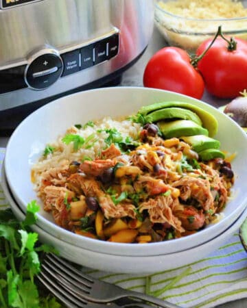 Chicken and black beans with rice and avocado, all in a white plate.