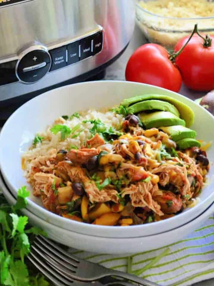 Chicken and black beans with rice and avocado, all in a white plate.