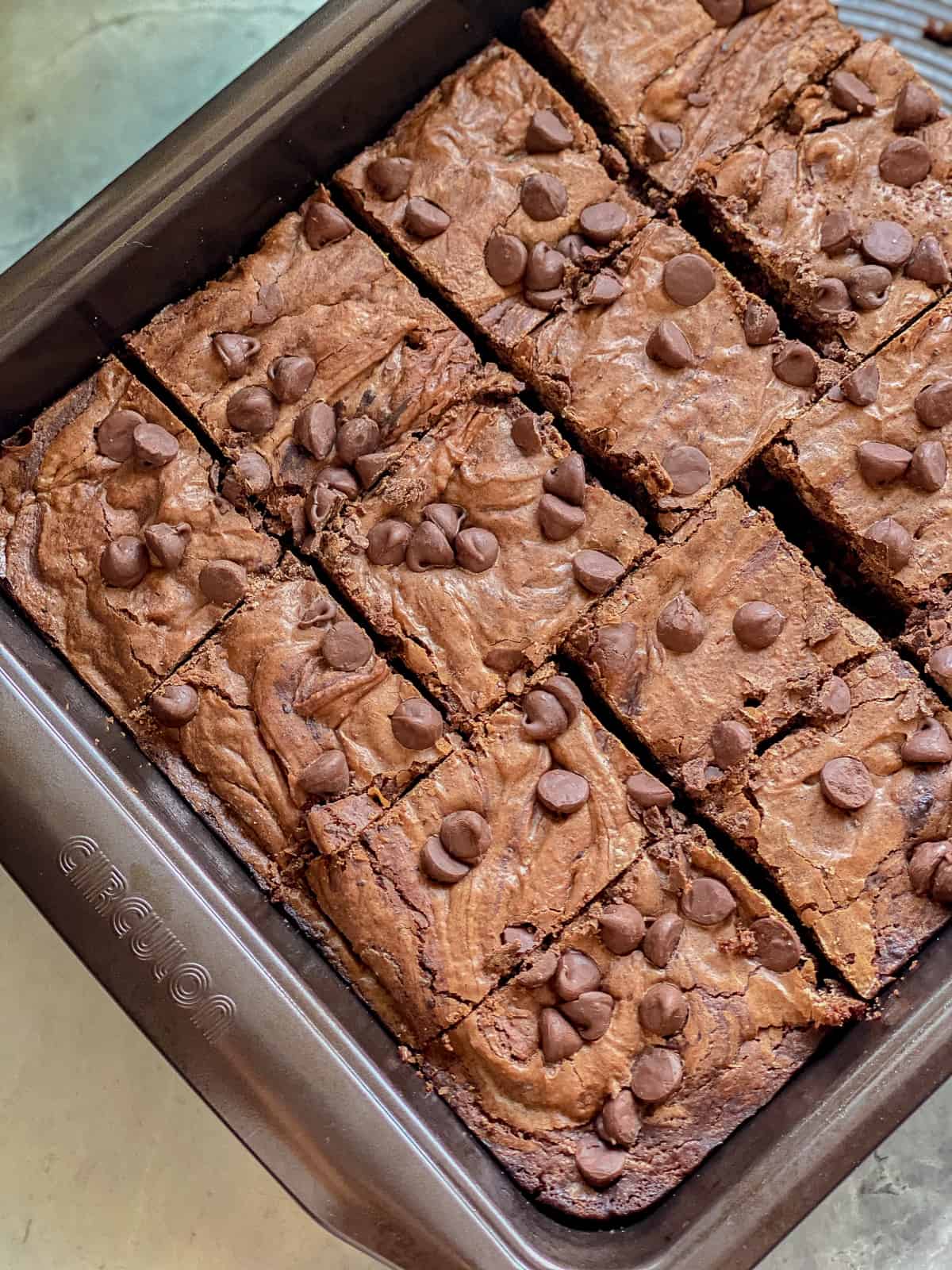 A brown pan with a brown brownie with brown chocolate chips on top on marble counter.