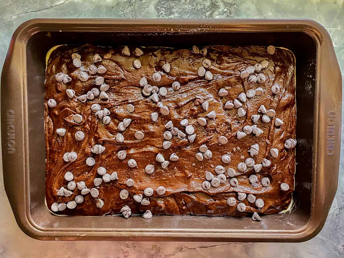 silver pan on marble counter with brown brownie mix with chocolate chips on top.