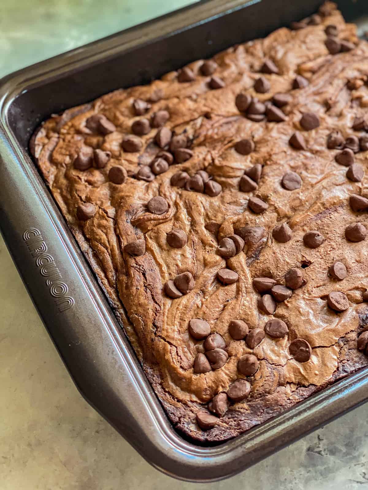 a close up of cooked brown chocolate brownies in a silver pan on a white marble counter