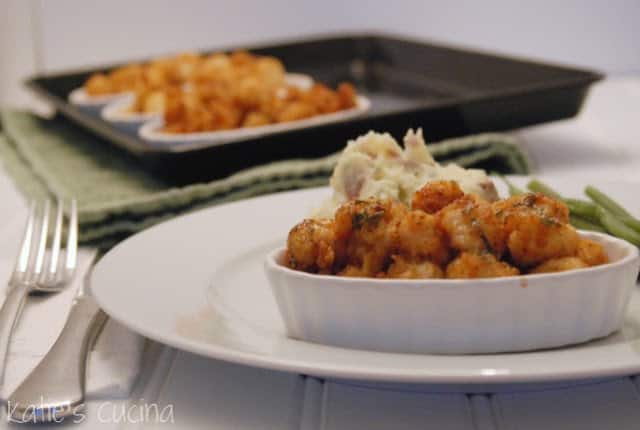 Oval white ramekin with bread scallops in dish on a plate with mashed potatoes and green beans.