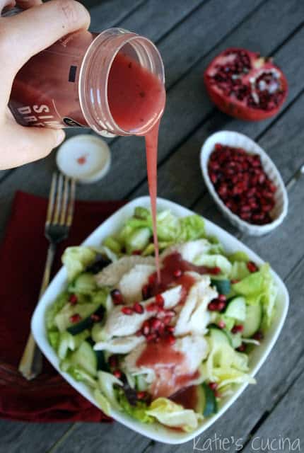 Hand pouring pink salad dressing over a white square bowl filled with lettuce and turkey.