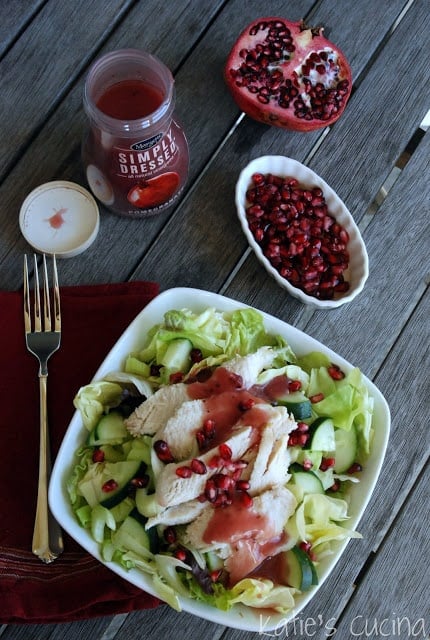 Top view of a square white salad bowl filled with salad, turkey, and pomegranates.