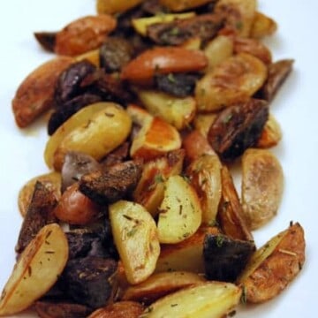 White dish with quartered roasted baby potatoes with herbs.