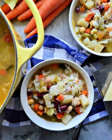 Top view of 2 bowls filled with minestrone soup topped with cheese on top of a checkered tablecloth.