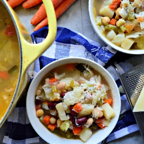 Top view of 2 bowls filled with minestrone soup topped with cheese on top of a checkered tablecloth.