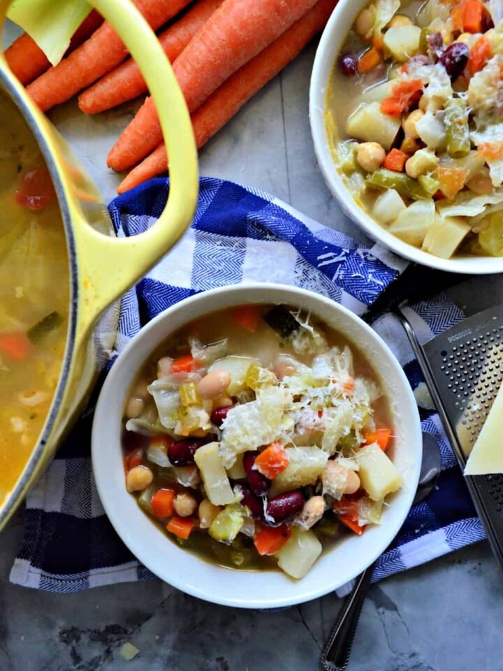 Top view of 2 bowls filled with minestrone soup topped with cheese on top of a checkered tablecloth.