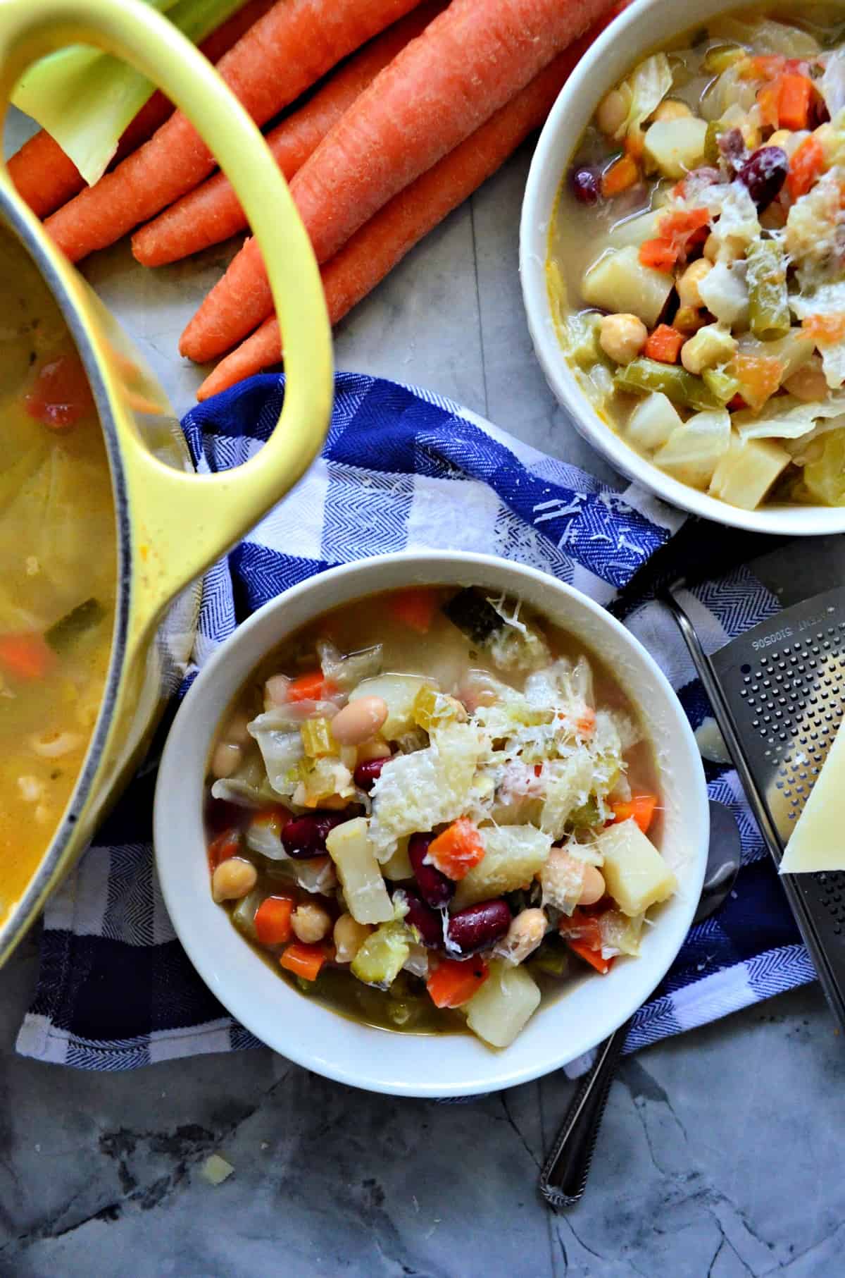 Top view of 2 bowls filled with minestrone soup topped with cheese on top of a checkered tablecloth.