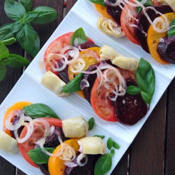 Top view of a plate filled with layered tomatoes, beets, onions, artichokes, and basil.