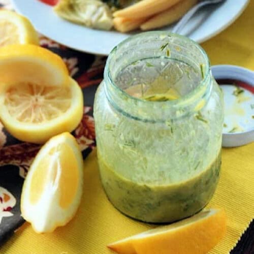 glass mason jar filled with dressing, lemons next to it on a yellow cloth placemat.
