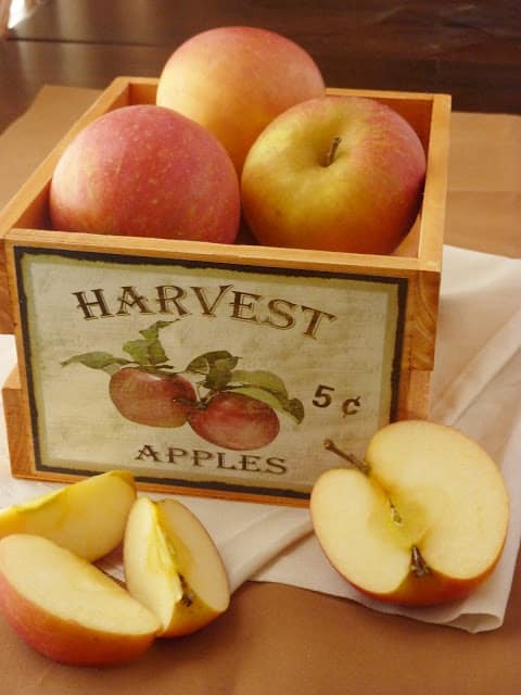 Basked of apples with an apple cut in half and in wedges in front of the basket.