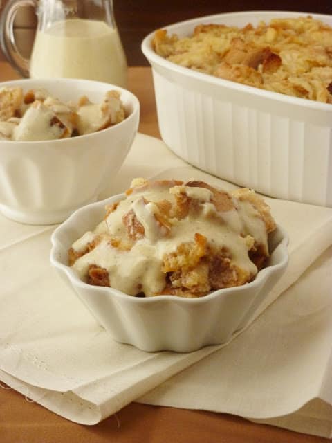 Two white bowls on a cream colored cloth filled with bread pudding and cream sauce.