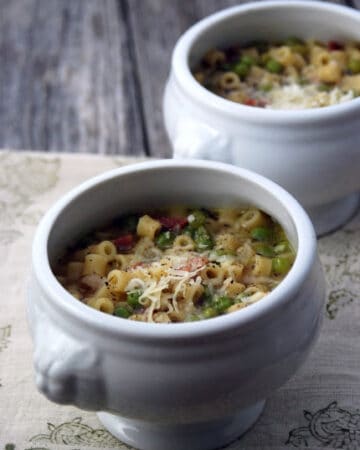 Two white urns full of peas, pasta, and meat in broth sittind on a wood board.