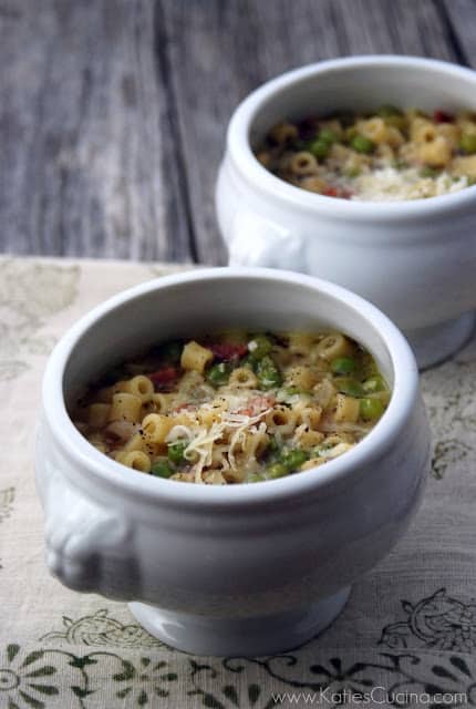 Two white urns full of peas, pasta, and meat in broth sittind on a wood board.