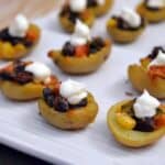Mini potato skins on a white plate filled with corn, black beans, and sour cream.