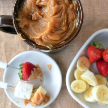 Mug of gooey caramel-colored substance next to plated items dipped in substance on fondue forks.