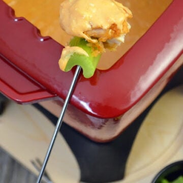Close up of red fondue pot with fondue fork being dipped into meldet cheese.