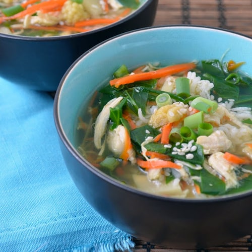 Two black bowls with blue interior with asian chicken rice soup inside.