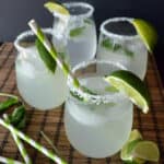 Four stemless wine glasses with salt onthe rim and limes with paper straws.