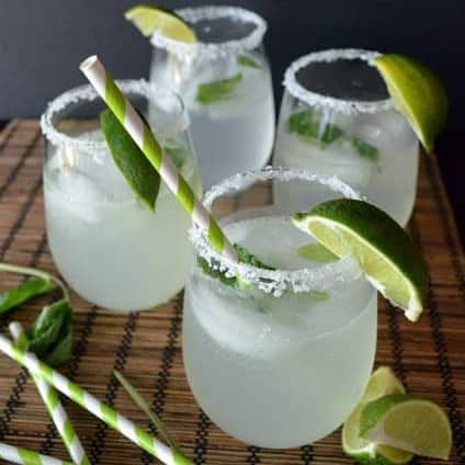 Four stemless wine glasses with salt onthe rim and limes with paper straws.