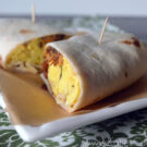 Plated burrito with eggs and meat sliced in half with toothpicks holding halves together.