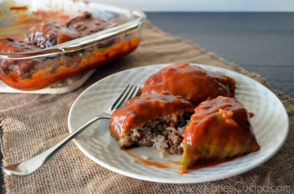 Plated meat-stuffed cabbage with red sauce glaze and fork on side.