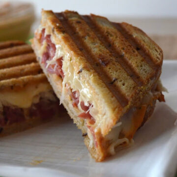 Plated sliced reuben sandwhich with sauce, sauerkraut, meat, and cheese displayed.