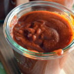 Glass filled with red spicy enchilada sauce.