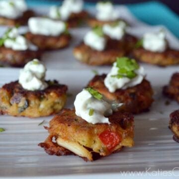 Close up of plated mini crab cakes topped with cilantro lime sauce dallop and cilantro leaf.