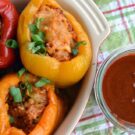 yellow, orange, and red stuffed bell peppers with green onion garnish and enchilada sauce on the side.
