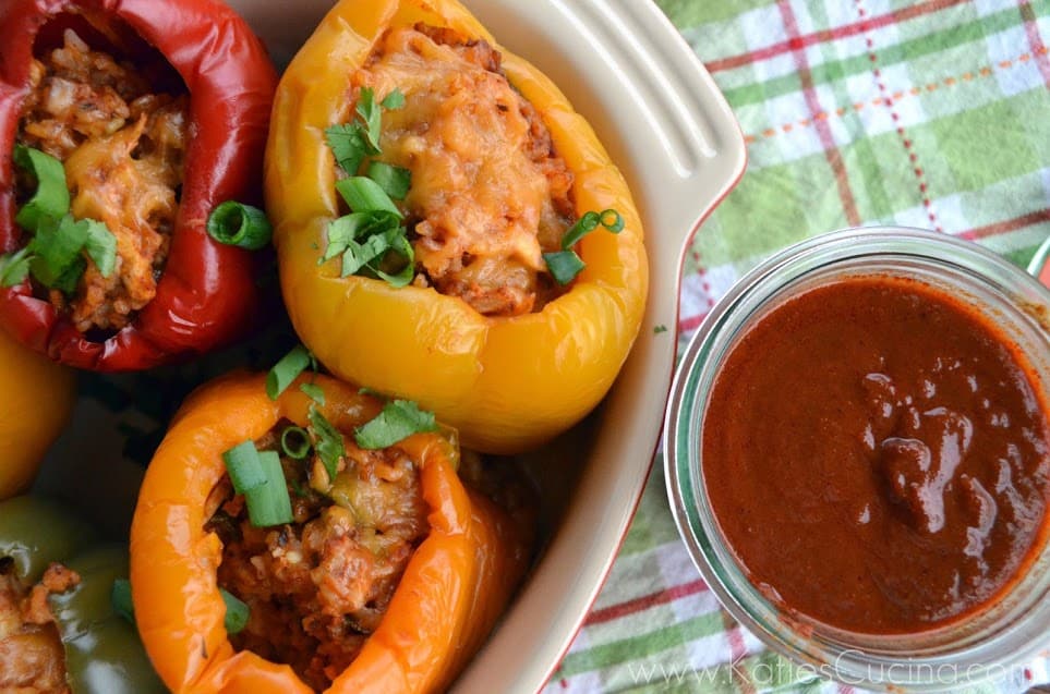 yellow, orange, and red stuffed bell peppers with green onion garnish and enchilada sauce on the side.