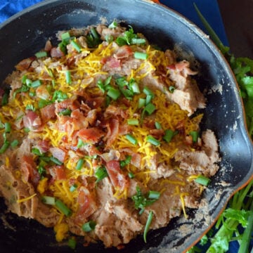 Top view of skilled filled with refried beans, green onions, bacon bits, and shredded cheese.