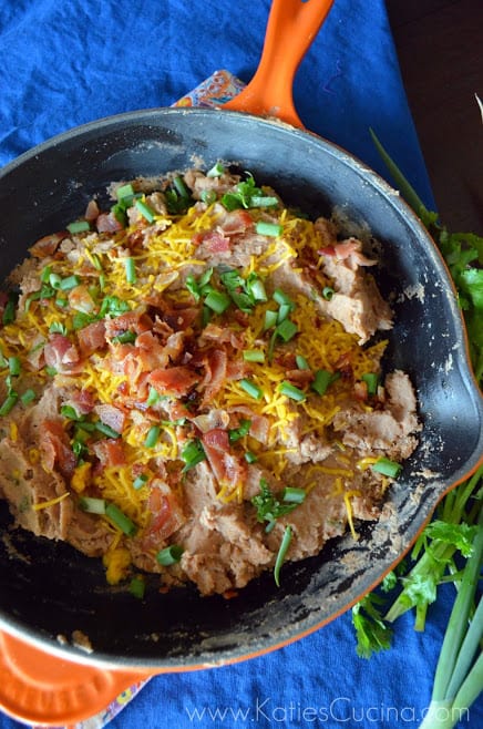 Top view of skilled filled with refried beans, green onions, bacon bits, and shredded cheese.