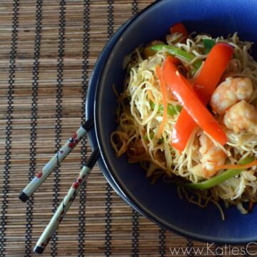 Bowl of Shrimp Veggie Lo Mein with chopsticks sticking out on bamboo placemat.